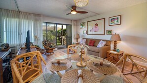 A well-lit living room with wicker furniture, a glass coffee table, and a ceiling fan. - KIHEI AKAHI CONDO STEPS FROM BEACH/GARDEN & PEEKABOO OCEAN VIEW/POOL-HOTEL ZONED (Kihei)