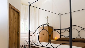 A room with a metal four-poster bed, a wooden wardrobe, a small table with a lamp, and a window with curtains. - Il Rifugio Pecorella (Alvignano)