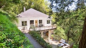 A house with a deck and a covered outdoor area, surrounded by dense greenery.