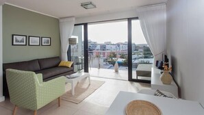 Un salón moderno con un sofá, un sillón verde, una mesa de centro y vistas de la ciudad a través de amplios ventanales.