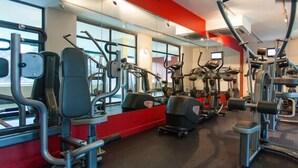 Un gimnasio con diversas máquinas de ejercicio, ventanas amplias y una pared de acento rojo.