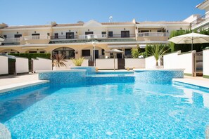Una piscina con bordo piastrellato, circondata da un muro bianco e un edificio con balconi.