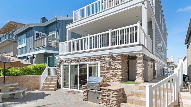 A two-story house with a balcony, stone foundation, and a barbecue area.