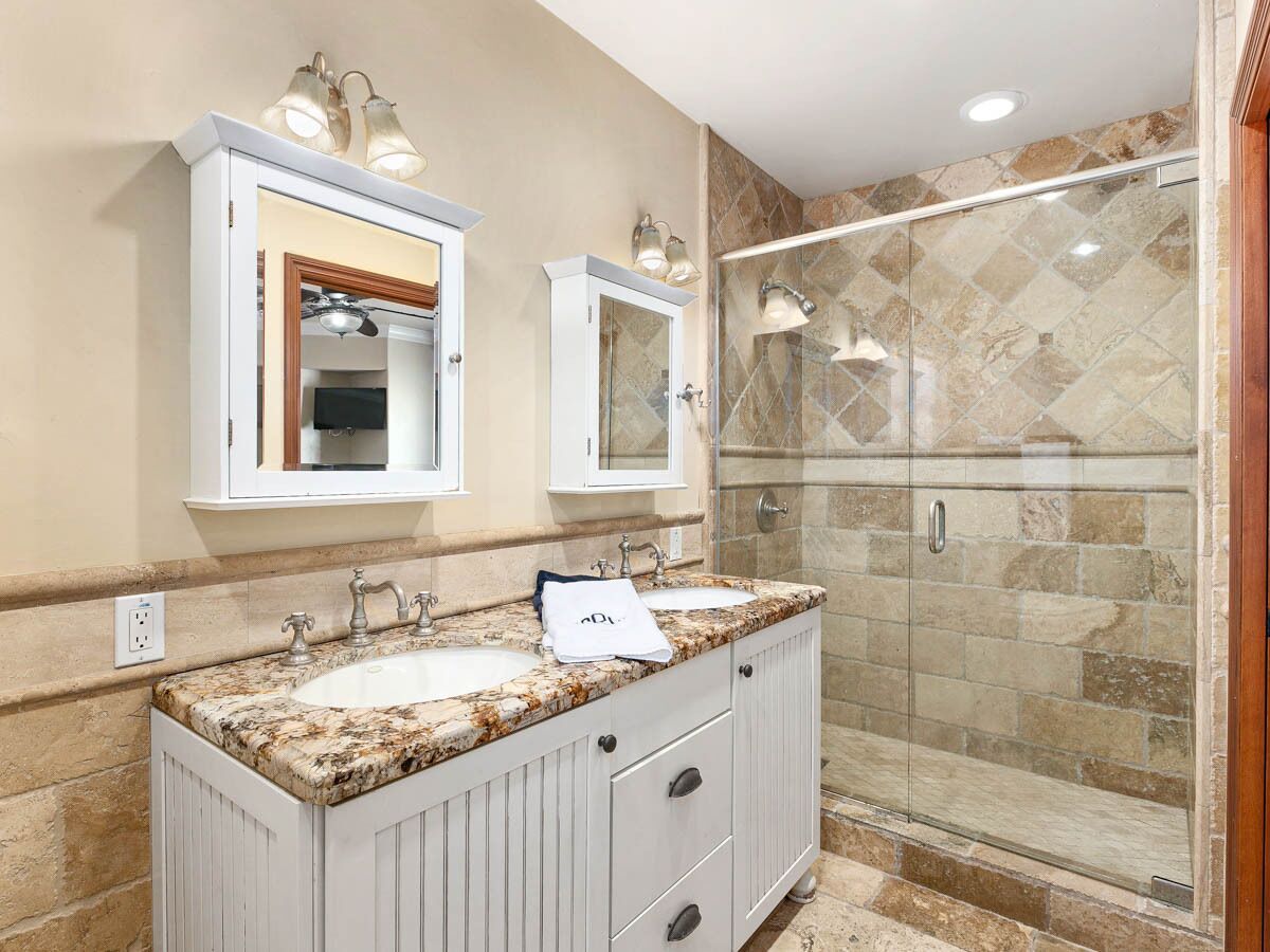 A bathroom with two sinks, a shower, and a glass-enclosed shower area.