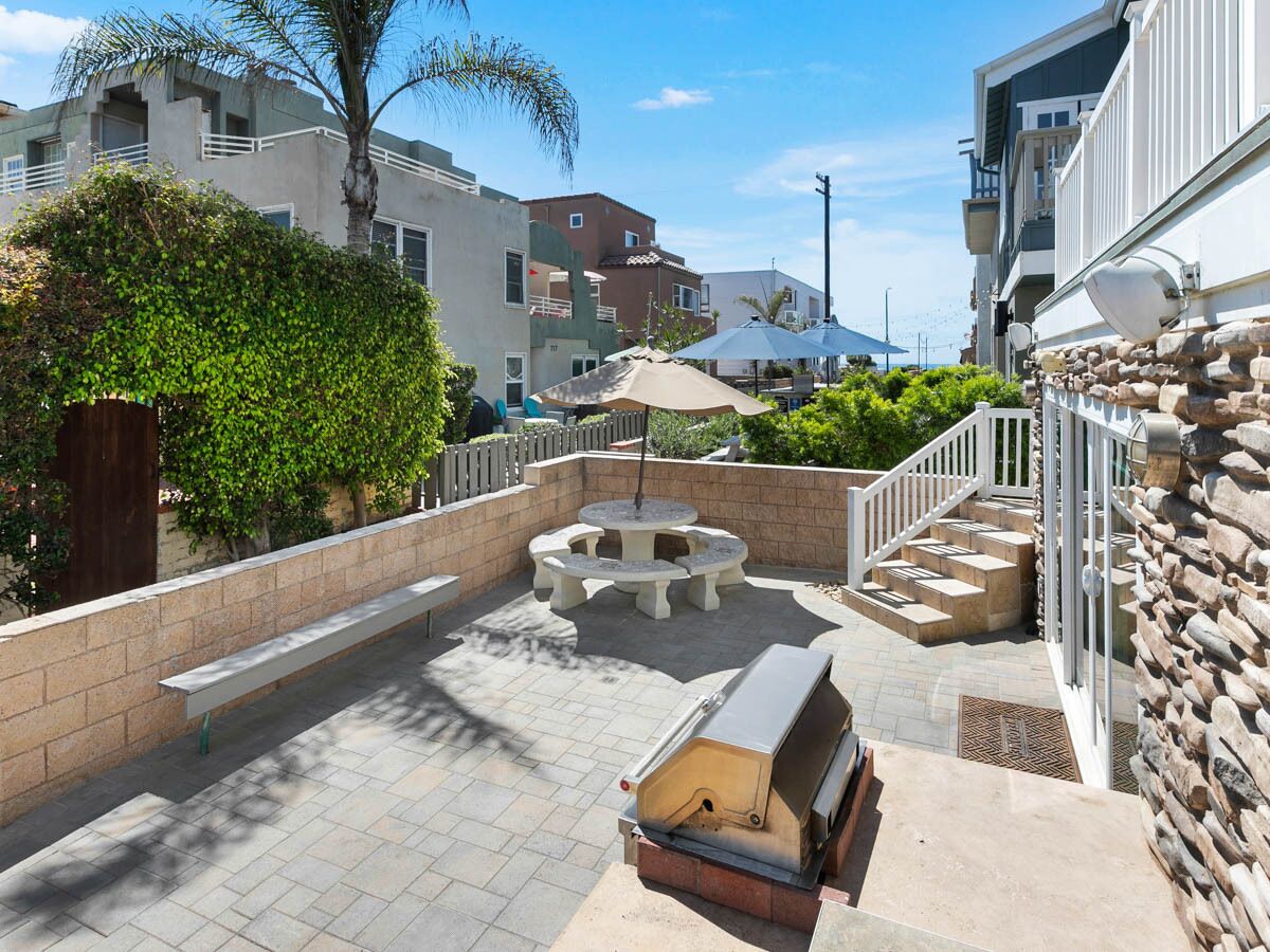 Un espace extérieur aménagé en patio, avec un barbecue, des sièges et un mur en pierre.
