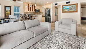 A modern living room with a large grey sofa, a smaller grey armchair, and a patterned rug.