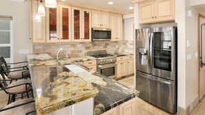 A modern kitchen with granite countertops, stainless steel appliances, and light wood cabinetry.