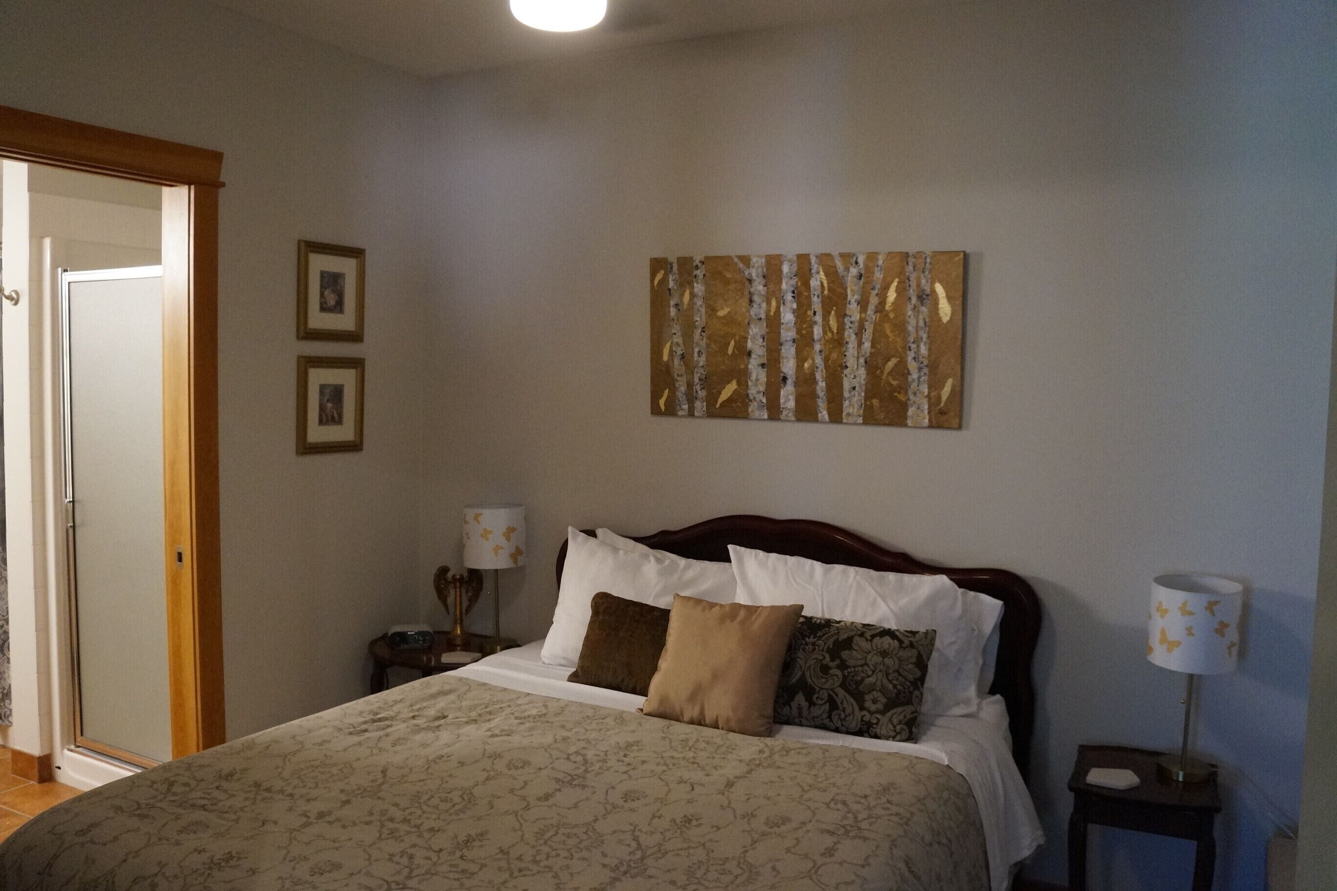 A neatly arranged bedroom with a bed, two bedside tables, a nightstand, and a wall-mounted artwork.