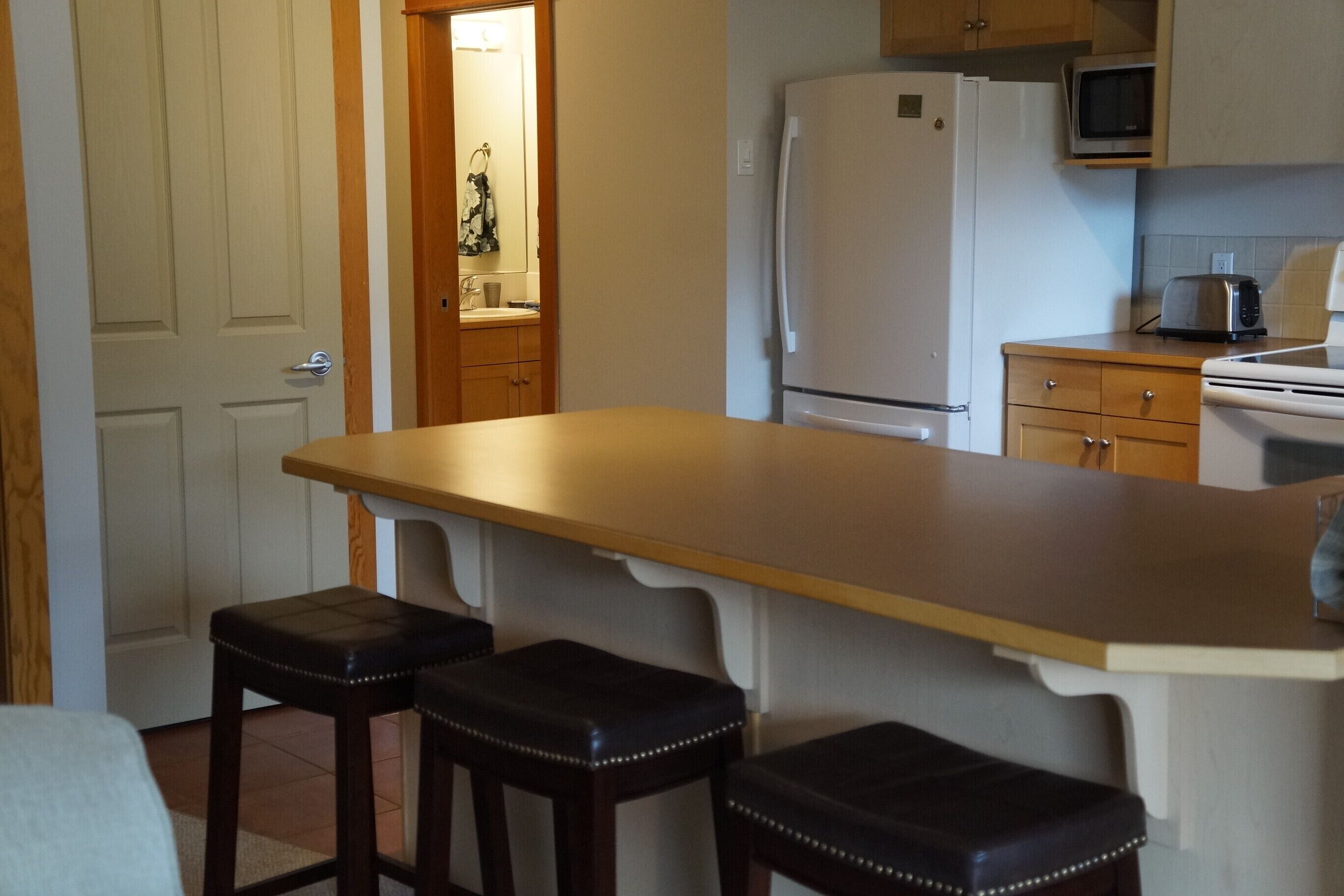 A kitchen with a wooden countertop, two stools, a refrigerator, a microwave, and a toaster.