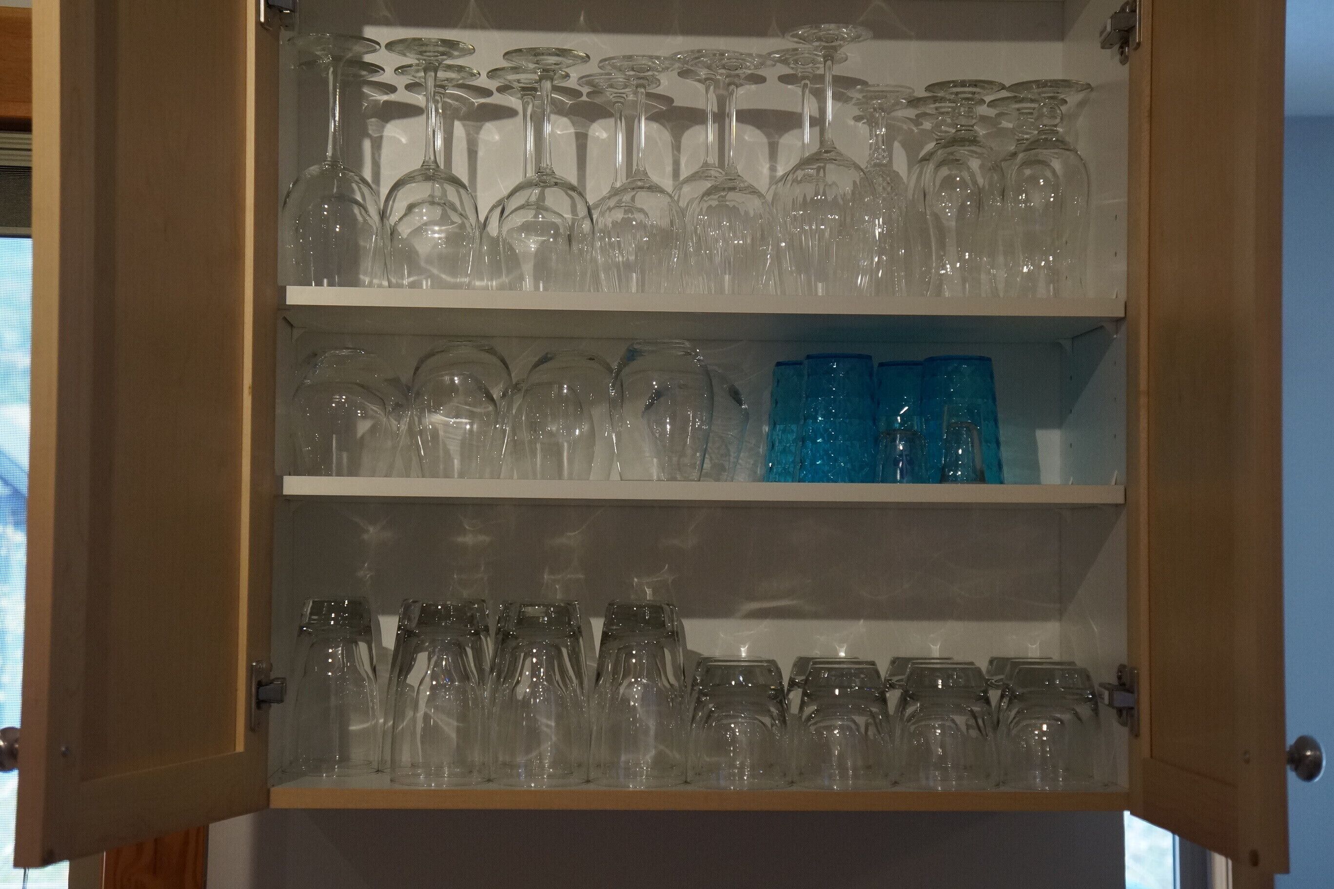 A cabinet with three shelves containing various glassware.