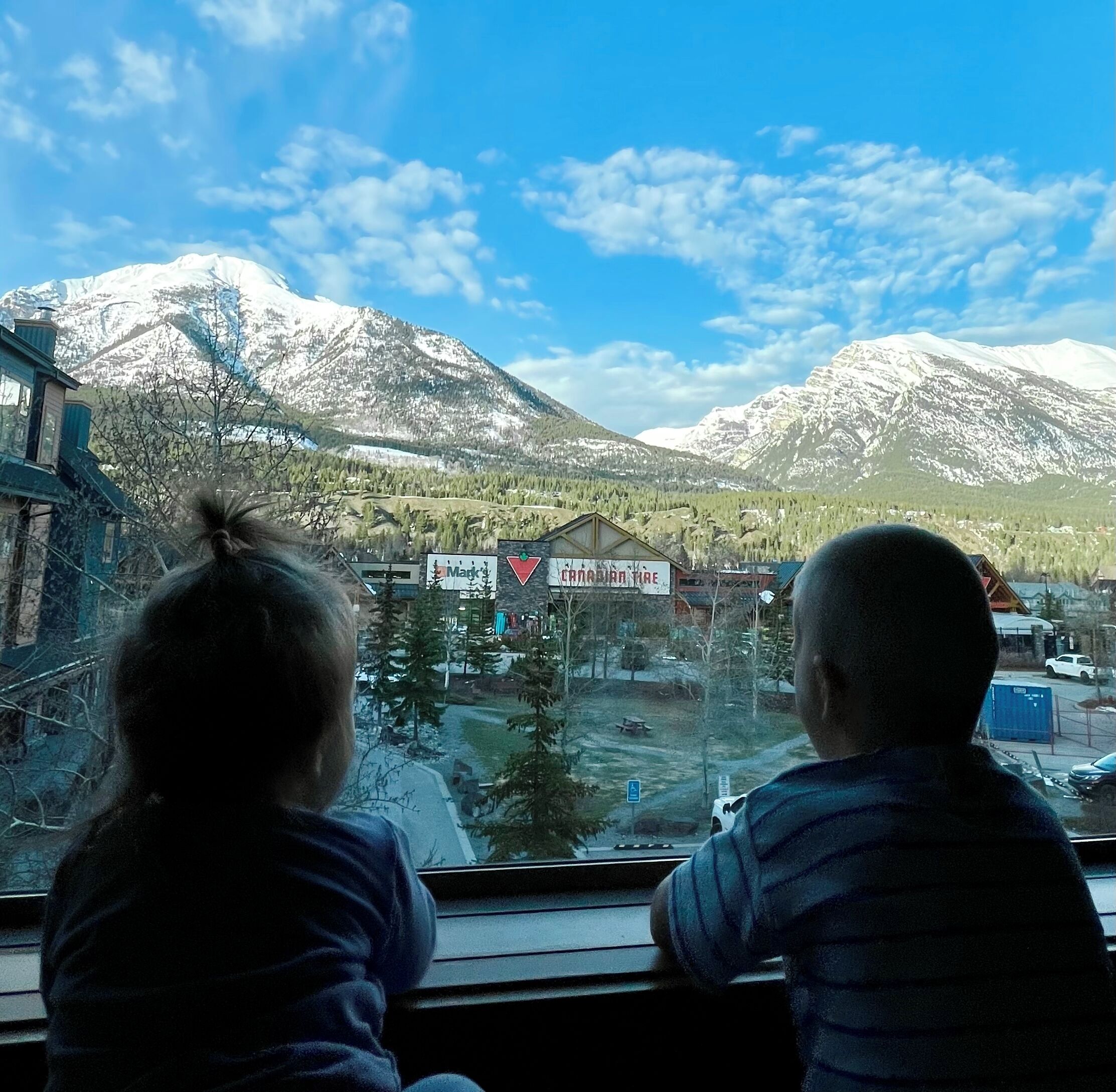 Two children looking out a window at a snowy mountain landscape with a small town in the foreground.