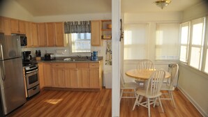Una cocina con armarios de madera, refrigerador, estufa y un comedor con mesa y sillas.