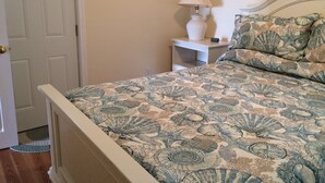 Un dormitorio con cama, mesita de noche, lámpara y puerta.