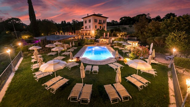 A pool area with lounge chairs and umbrellas, surrounded by a well-maintained lawn and a large building in the background. - Domus Volumnia Country House (Perugia)