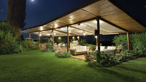 An outdoor covered patio area with a wooden roof, furnished with a sofa and chairs, surrounded by greenery and a view of the night sky. - Domus Volumnia Country House (Perugia)