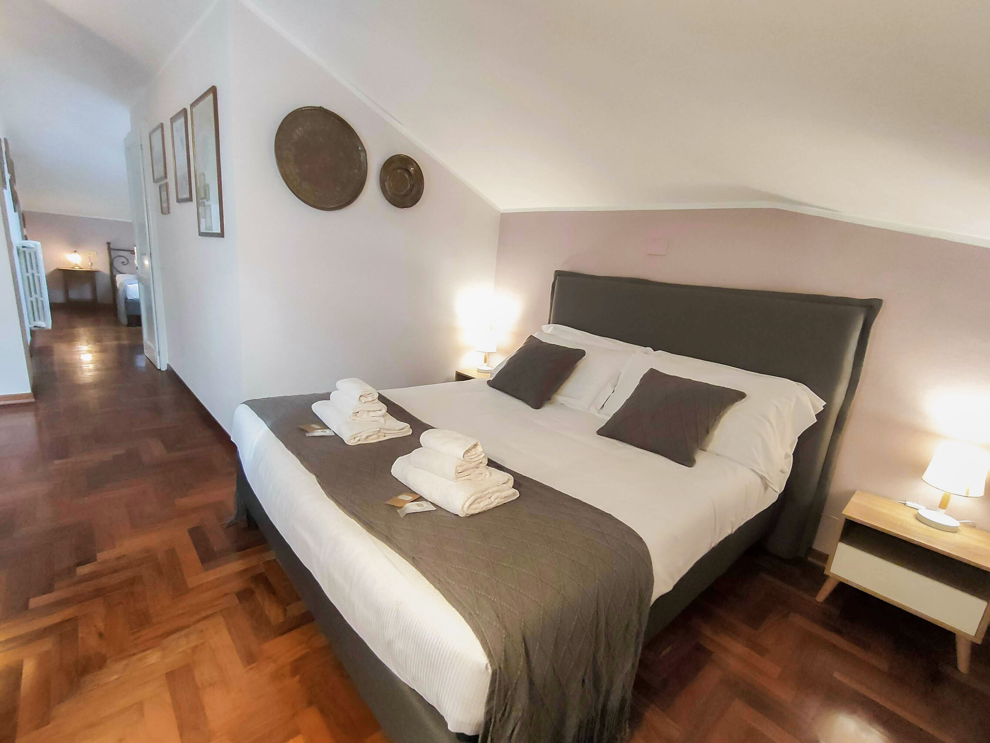 Quarto de hotel com uma cama grande, mesa de cabeceira com abajur e piso de madeira.