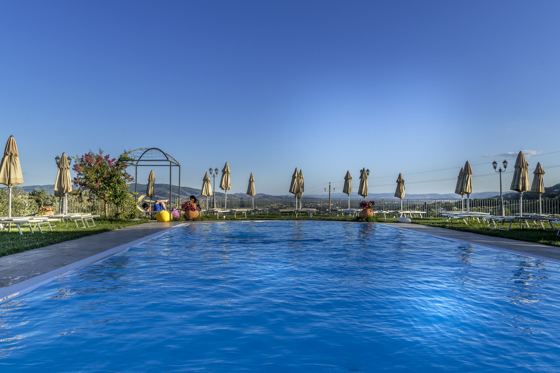 Una piscina con cielo azul despejado, rodeada de sillas de descanso y sombrillas.