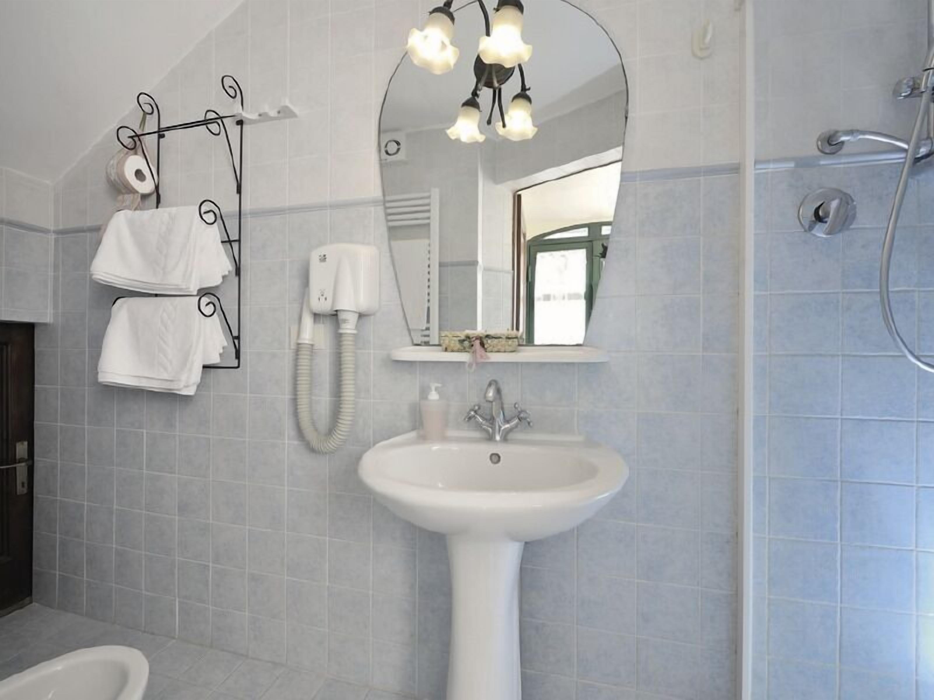 Ein Badezimmer mit einem weißen Waschbecken, einem Spiegel, einem Handtuchhalter mit Handtüchern, einer Handbrause und einer Toilette.