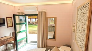 A bedroom with a bed, bedside table, and a desk. There is a window with curtains, an air conditioning unit, and a decorative wall panel. - Domus Volumnia Country House (Perugia)
