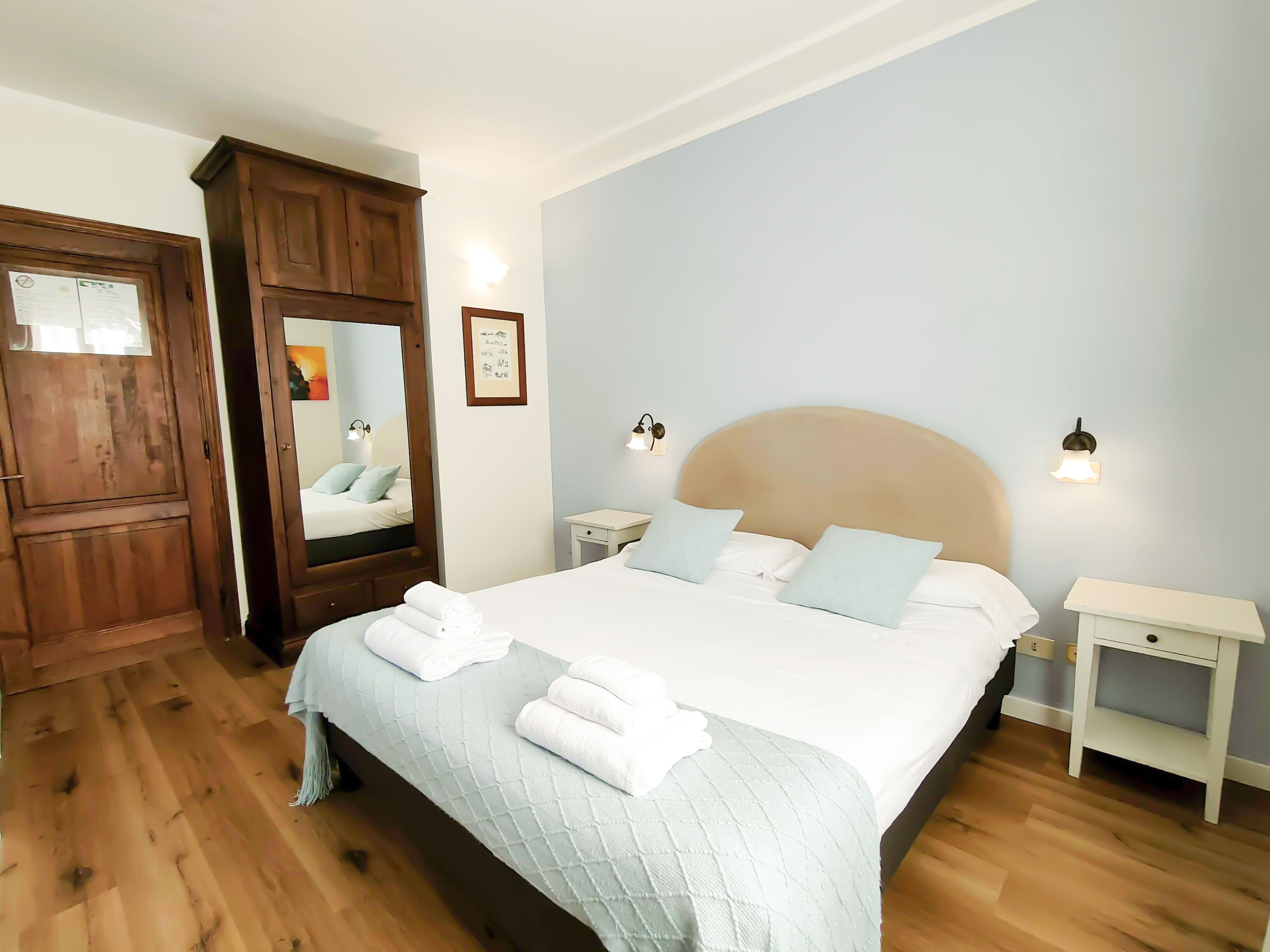 A bedroom with a large bed, wooden wardrobe, and bedside tables.