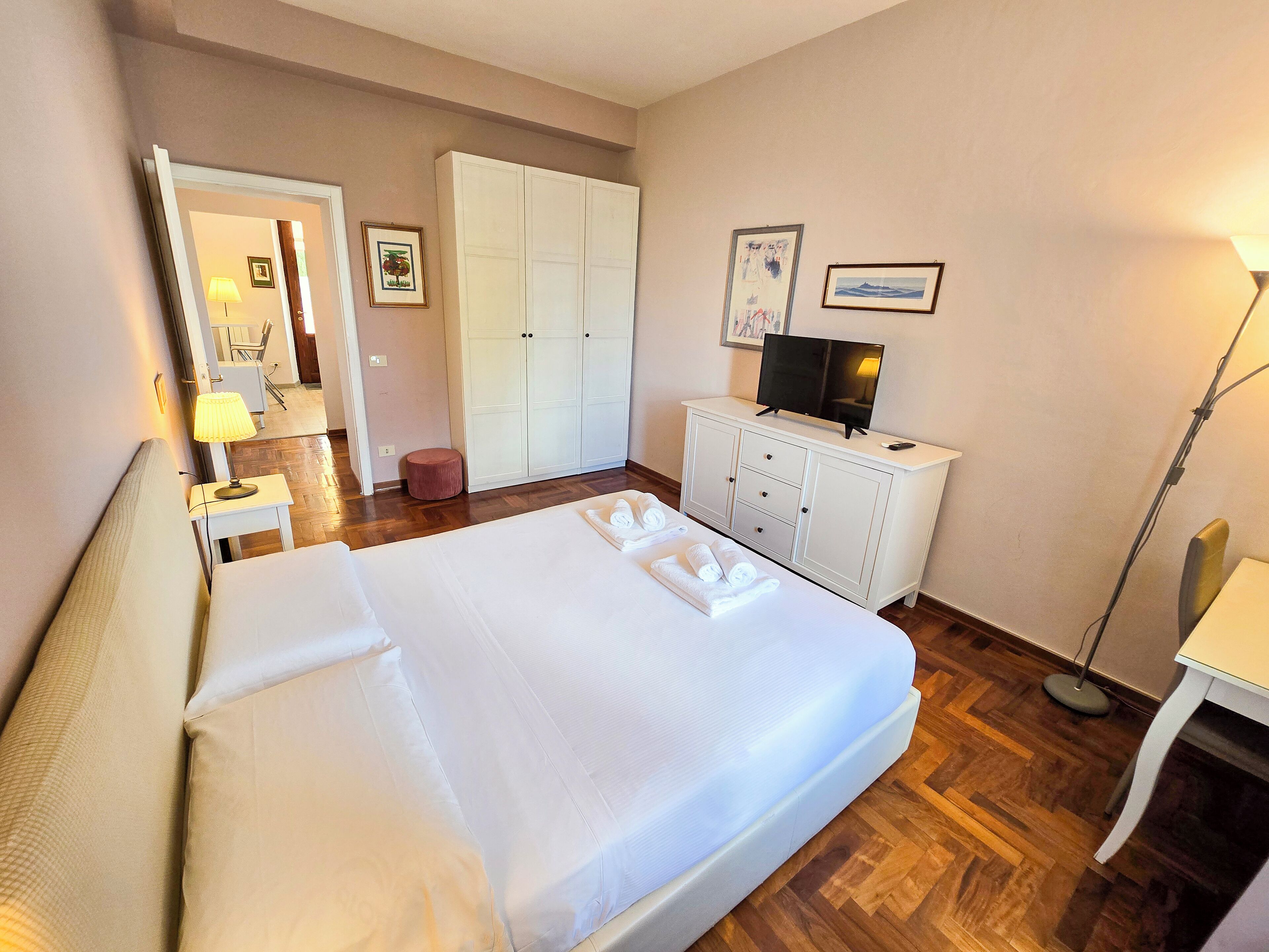 Ein Hotelzimmer mit einem großen Bett, einem Kleiderschrank, einem Fernseher und einem Schreibtisch mit Lampe.