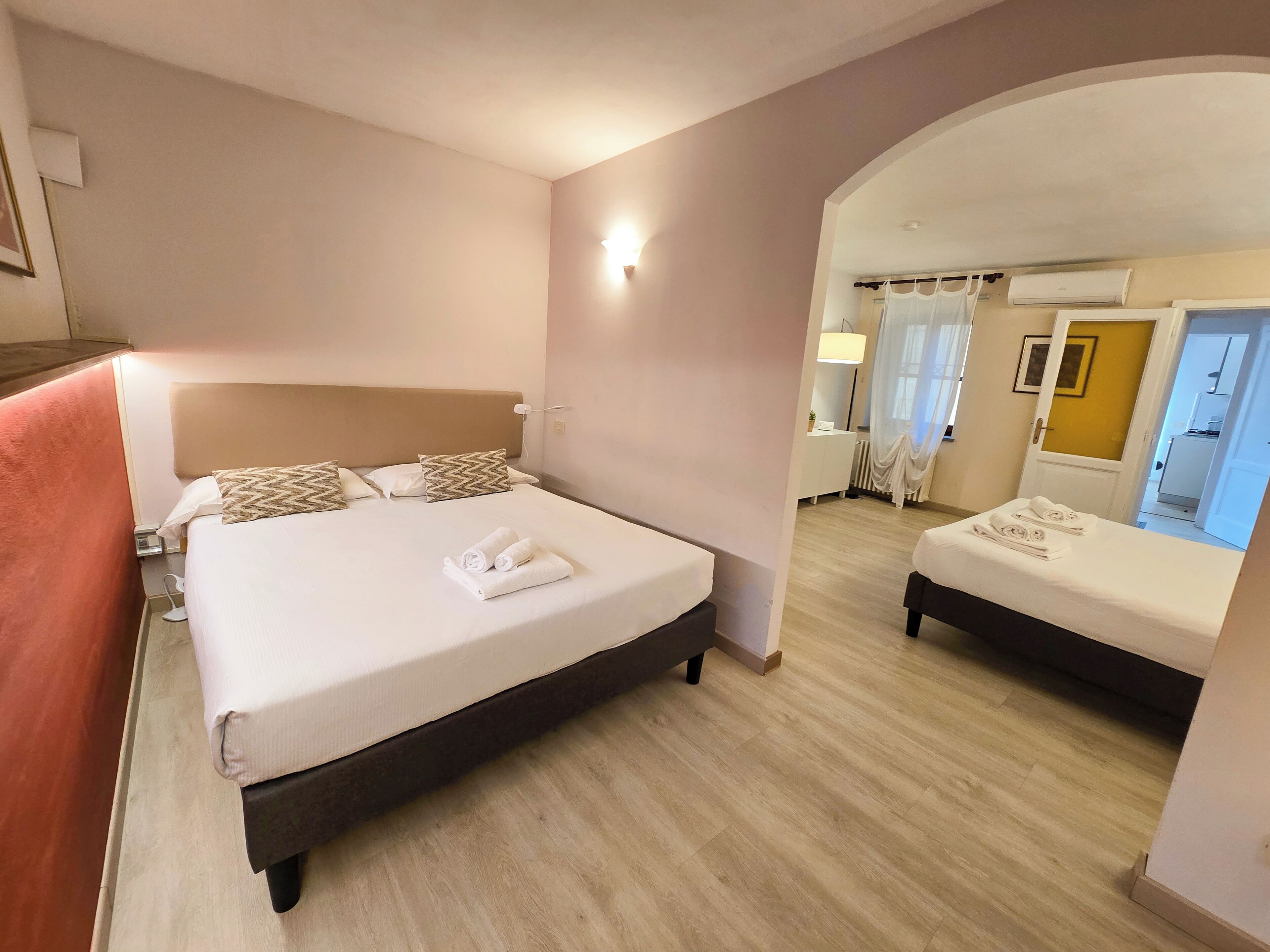 Habitación de hotel con una cama grande, una cama más pequeña y un baño visible a través de un arco.