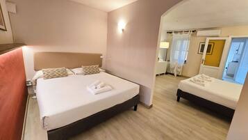 Habitación de hotel con una cama grande, una cama más pequeña y un baño visible a través de un arco.