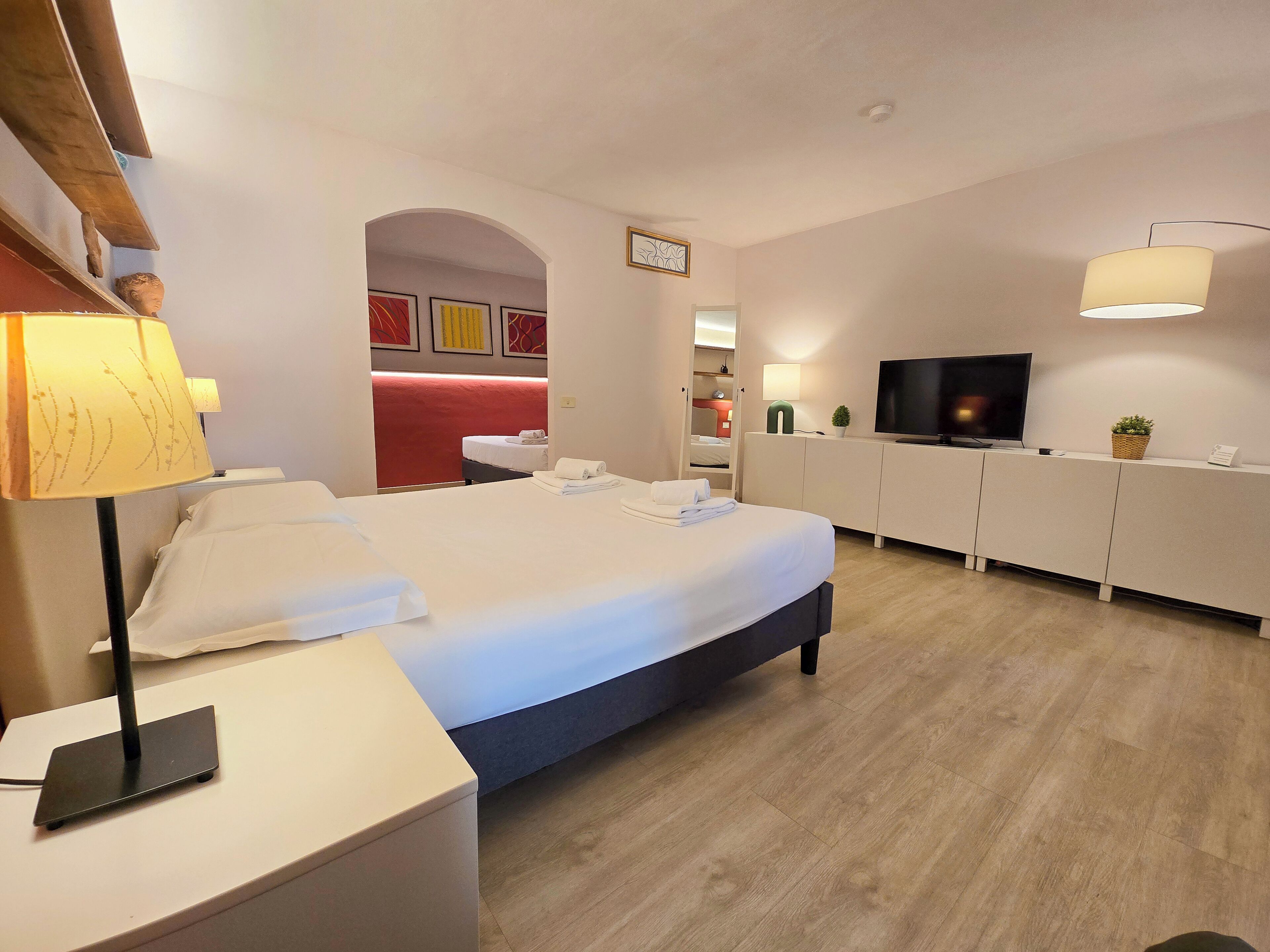Habitación de hotel con cama, mesita de noche, lámpara, televisor y una pequeña planta.