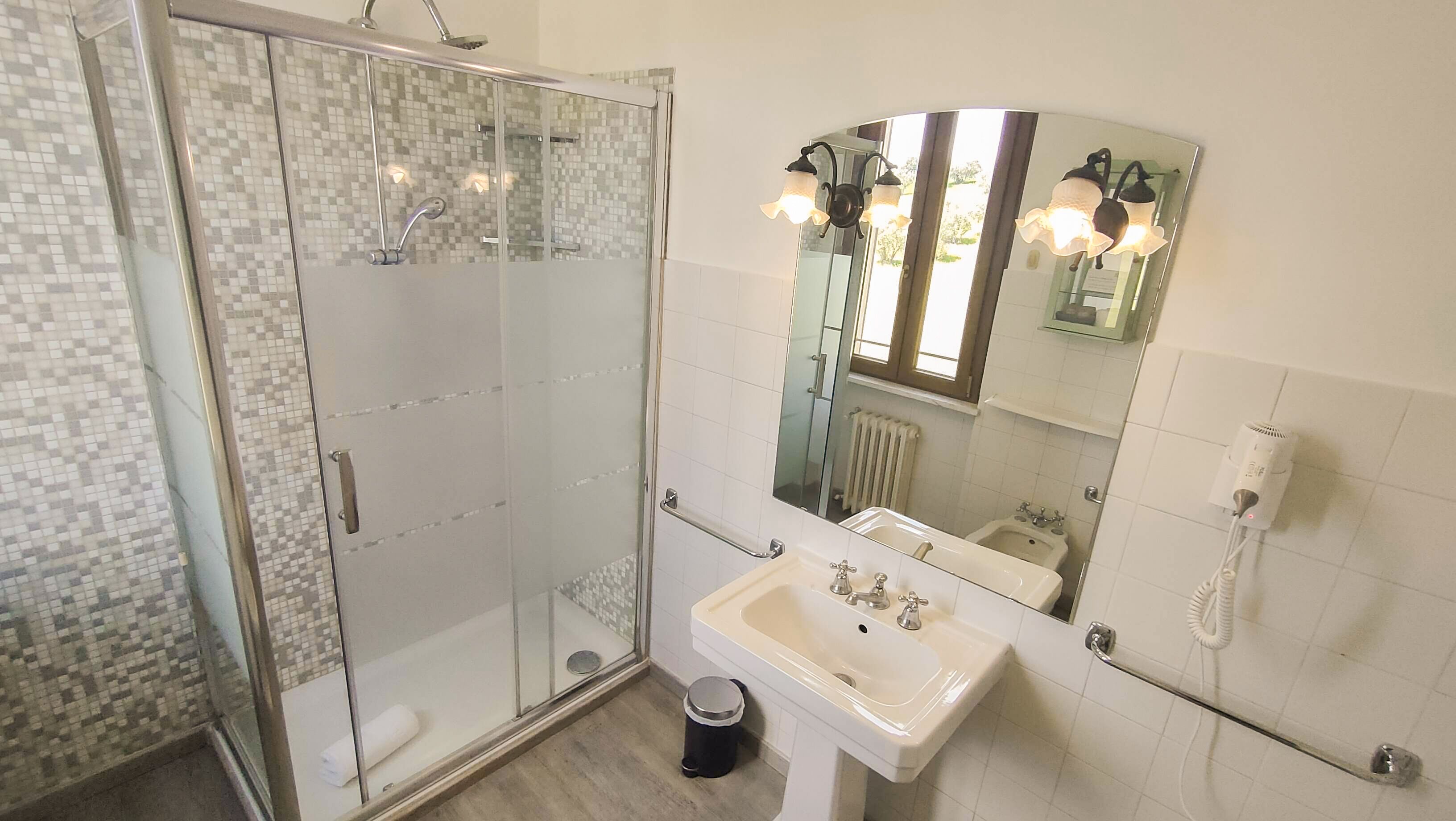 Ein modernes Badezimmer mit Duschkabine, Waschbecken und Spiegel sowie einem Haartrockner an der Wand.
