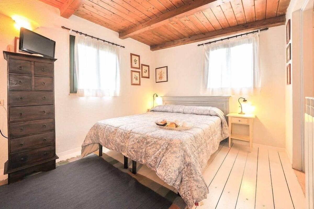 A bedroom with a bed, a dresser, two bedside tables with lamps, and a television on a dresser.