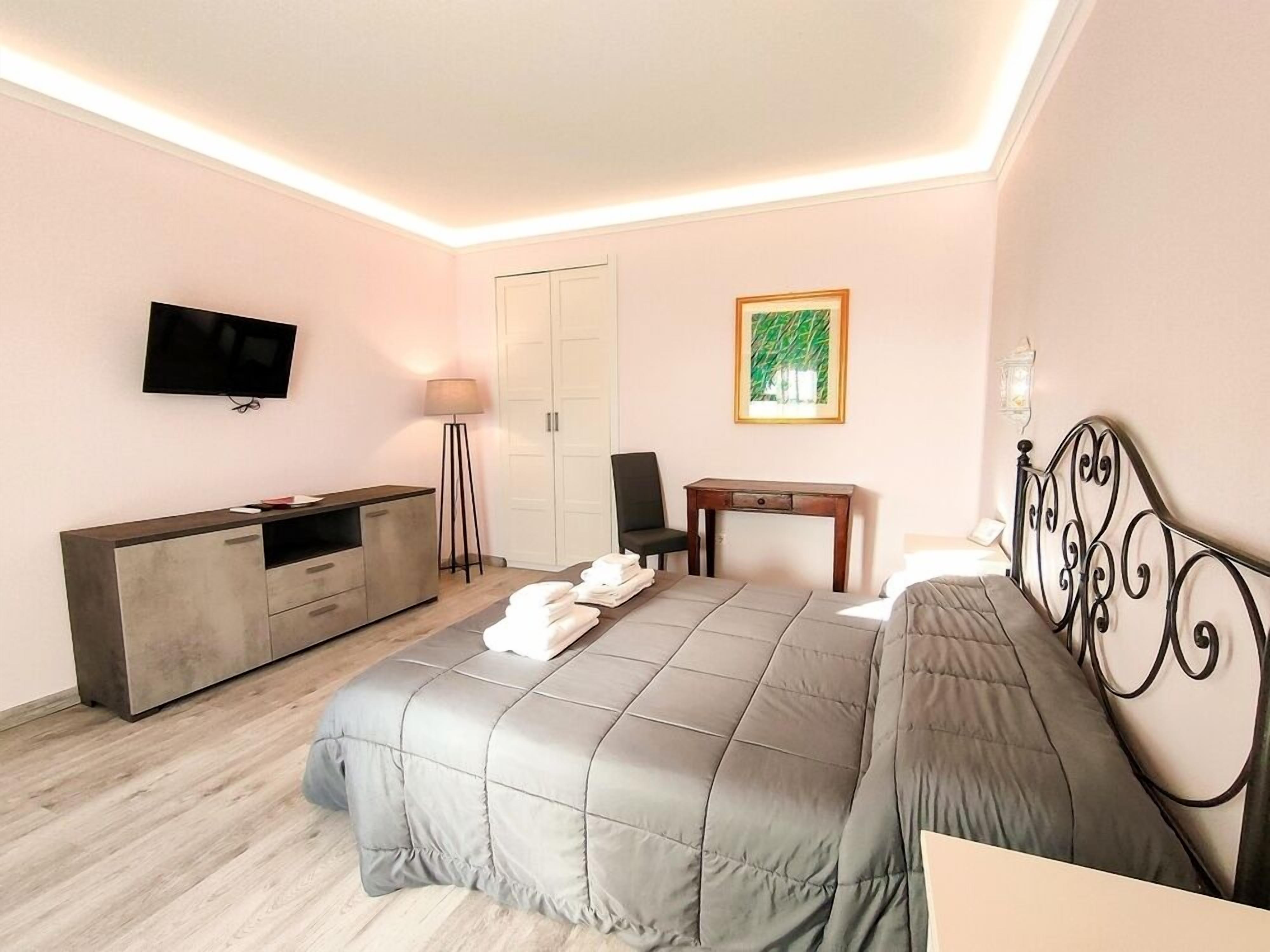 A modern hotel room with a bed, a desk, a TV, a wardrobe, and a painting on the wall.