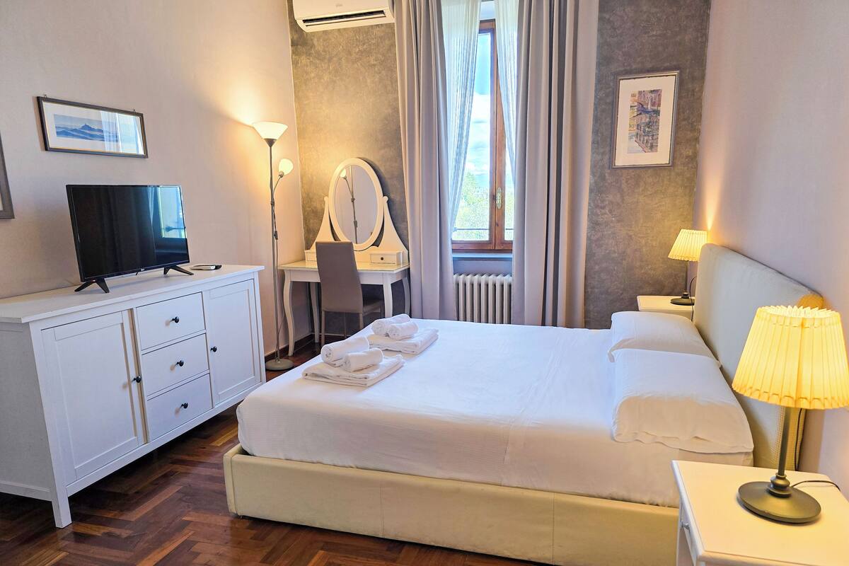 A hotel room with a bed, a desk, a chair, a television, and a window with curtains.