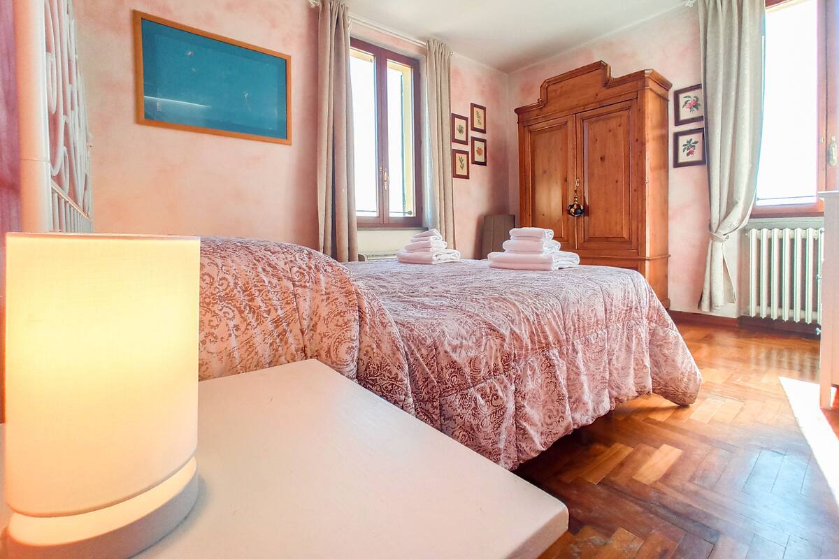 A bedroom with a bed, a bedside table, a wooden wardrobe, and a window with curtains.