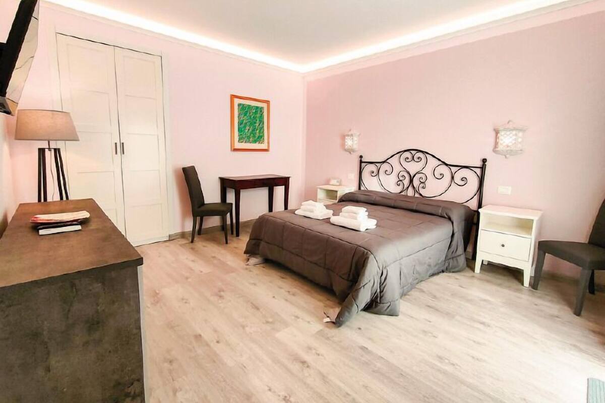 A bedroom with a bed, bedside tables, a desk, a chair, a lamp, and a wardrobe.