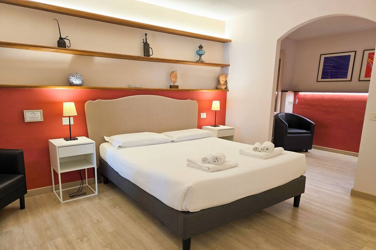 A hotel room with a bed, two bedside tables with lamps, a chair, and a shelf with decorative items.