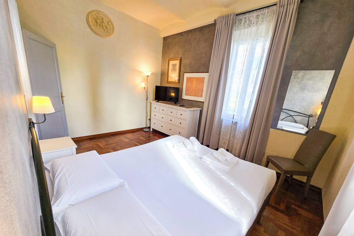 A hotel room with a large bed, a desk with a computer, a chair, and a window with curtains.