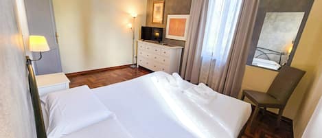 A hotel room with a large bed, a desk with a computer, a chair, and a window with curtains.