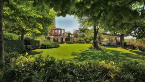 A lush garden with a gazebo, a reception area, and a building with a red facade. - Domus Volumnia Country House (Perugia)