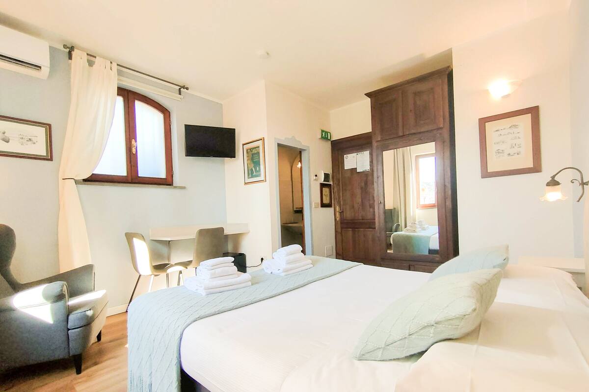 A hotel room with a bed, a chair, a desk, a flat-screen TV, and a mirror.