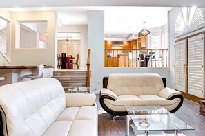 A modern living room with a sofa, a glass coffee table, and a dining area with wooden cabinets and a staircase.