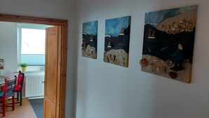 Una habitación con techo de madera, paredes blancas y tres cuadros que representan paisajes.