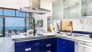 Une cuisine moderne avec des armoires bleues, des appareils en acier inoxydable et une grande fenêtre donnant sur l’océan.