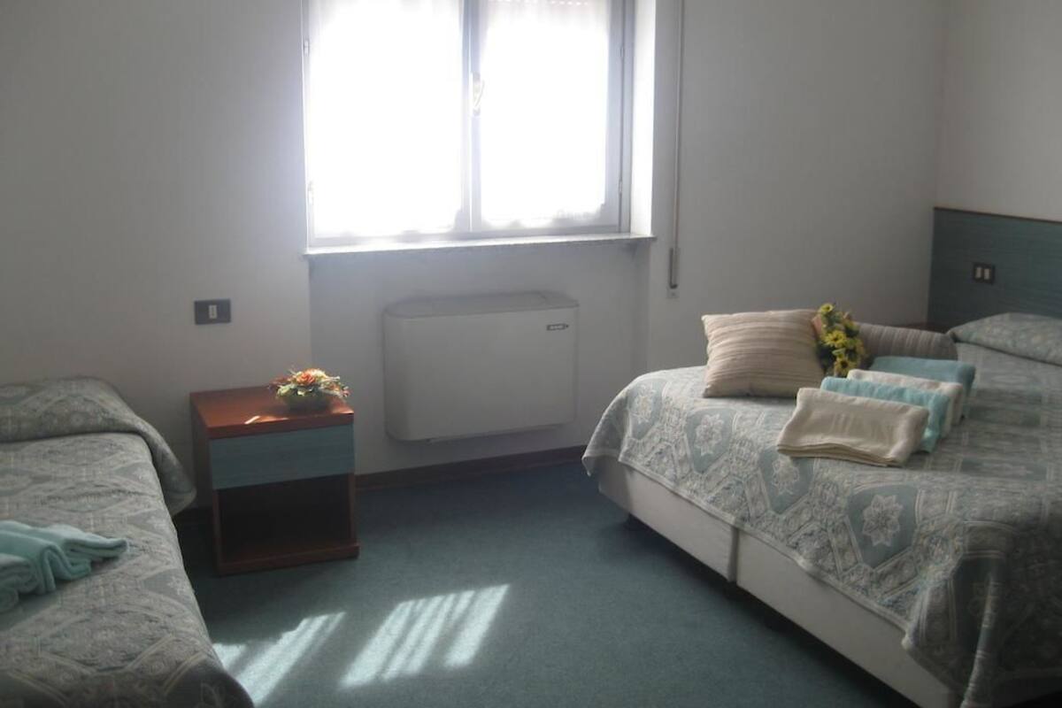 A bedroom with a bed, a nightstand, a window, and a radiator.