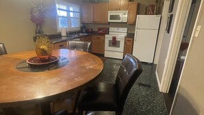 A kitchen with wooden cabinets, a microwave, a stove, and a refrigerator. There is a dining table with chairs and a vase with flowers.