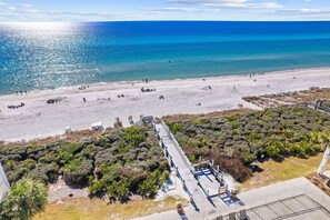 A beach with a wooden walkway leading to a building, surrounded by dense vegetation.