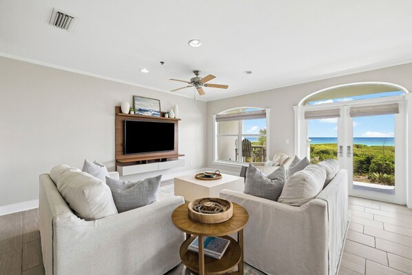 A living room with a TV, sofas, a coffee table, and a view of the ocean.
