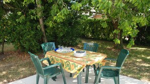 An outdoor dining area with a table and chairs, surrounded by trees.
