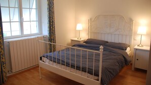 A bedroom with a white metal bed frame, two bedside tables with lamps, a radiator, and a window with curtains.