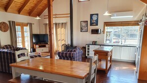 Un salon confortable avec une table et des chaises en bois, un téléviseur et un canapé. Il y a également un coin cuisine équipé d’un four à micro-ondes et de placards.