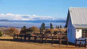 Un bâtiment blanc avec un toit en pente, une clôture en bois et une vue sur des montagnes enneigées au loin.